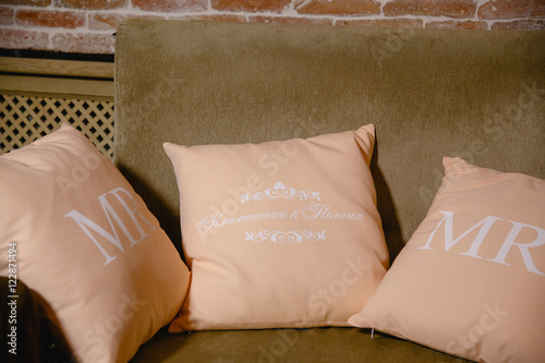 Pink pillows with initial letters lie on a brown sofa
