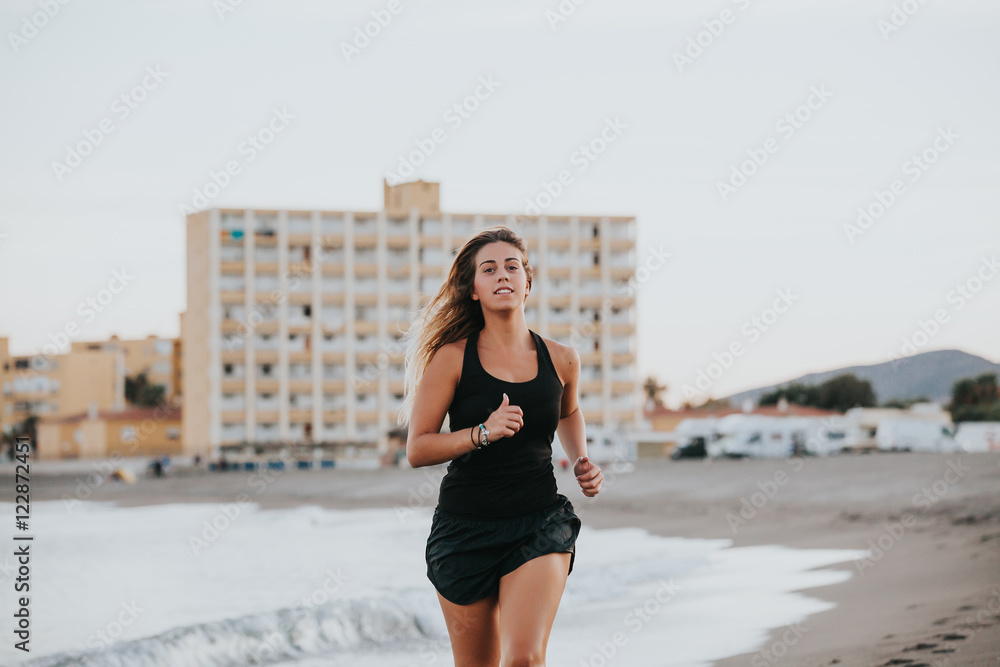 Blonde woman running in the beach with black sportswear.