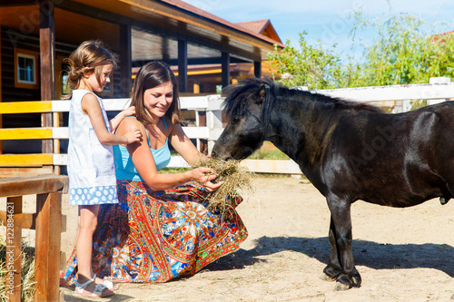 Mother and daughter are fed with straw ponies on the farm. photo