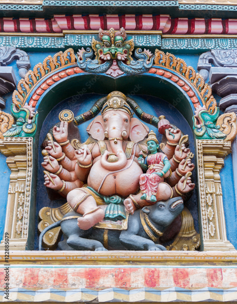 Madurai, India - October 19, 2013: Closeup of Lord Ganesha with his wife Devi Riddhi on his knee. He sits on his mount the rat and has multiple arms. Facade of Nagara Mandapam.
