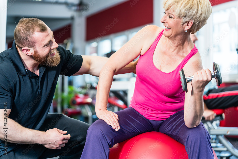 senior Frau beim Hanteltraining mit Fitnesstrainer im Fitnessstudio senior Frau beim Hanteltraining mit Fitnesstrainer im Fitnessstudio