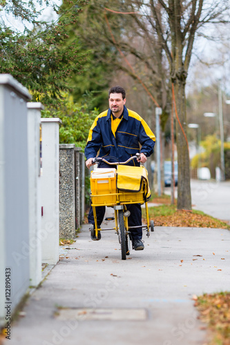 Briefträger fährt auf seinem Lastenfahrrad Post in Wohngebiet aus  photo