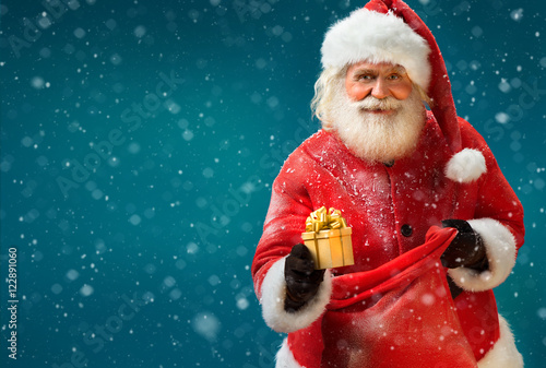 Happy Santa Claus with gift on blue background. Merry Christmas & New Year's Eve concept. photo