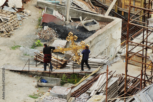 people carry a large golden Orthodox cross against the backdrop of the temple construction
