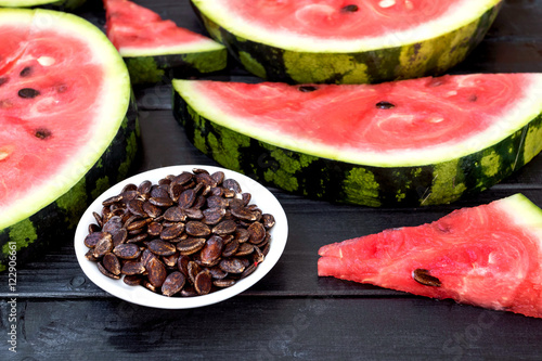 Background of fresh ripe watermelon slices and watermelon seeds on black wooden table. Close up.