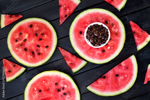 Background of fresh ripe watermelon slices and watermelon seeds on black wooden table. Top view.