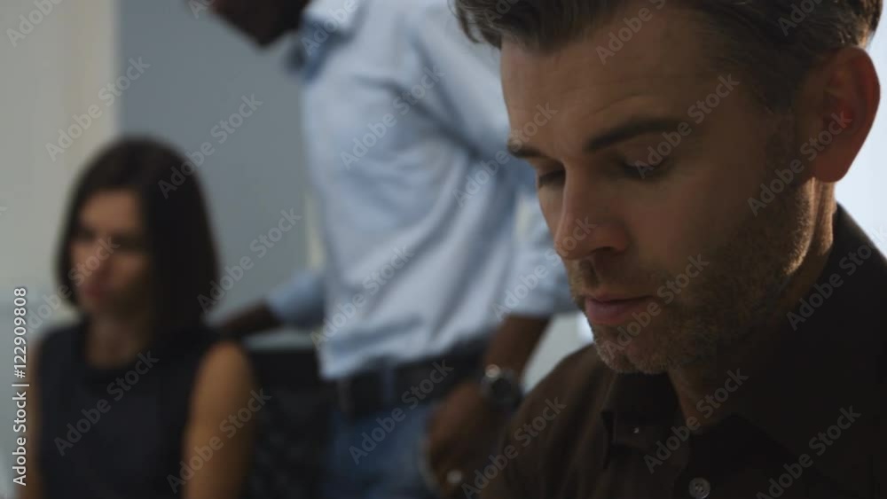 Handsome serious man working in an his office, while his colleagues discussing new project. Handsome serious man working in an his office, while his colleagues discussing new project.