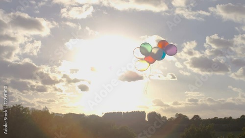 Young child releases all her balloons as they float into the sky, in slow motion photo