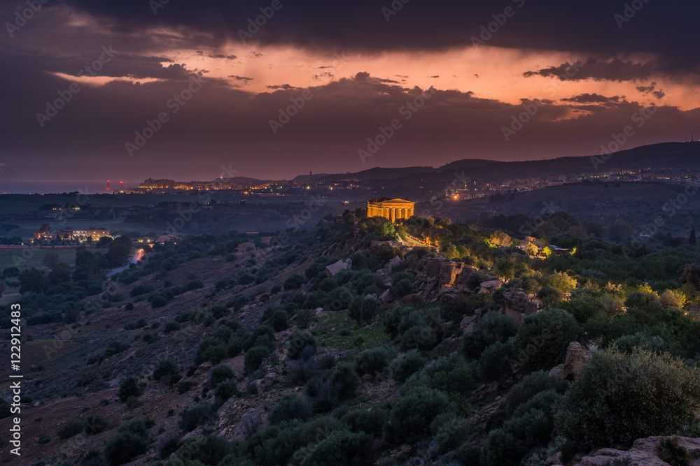 Sunset in Valley of temples in Agrigento in Sicily with clouds and night illumination.