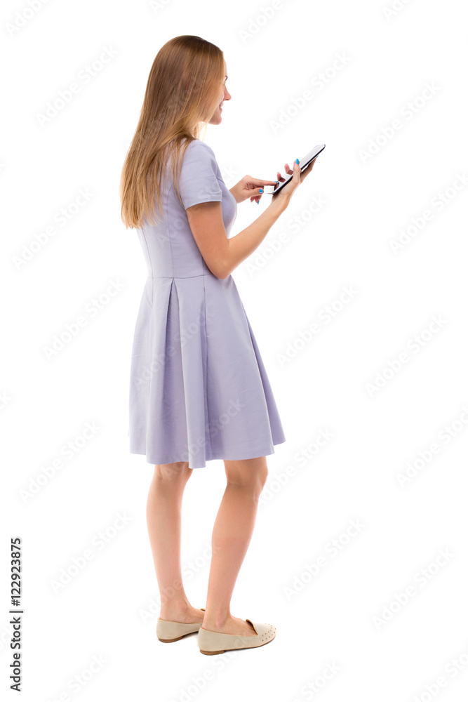 back view of standing young beautiful girl with tablet computer in the hands of. girl watching. Rear view people collection. backside view of person. Isolated over white background.Skinny girl in back view of standing young beautiful girl with tablet computer in the hands of. girl watching. Rear view people collection. backside view of person. Isolated over white background.Skinny girl in