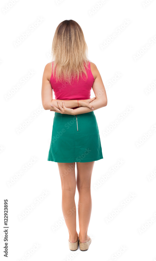 Naklejka premium back view of standing young beautiful woman. girl watching. Rear view people collection. backside view of person. Girl in green skirt standing with her hands folded on her back