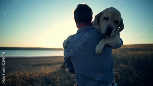 back view of man carrying old dog in sun light slow motion