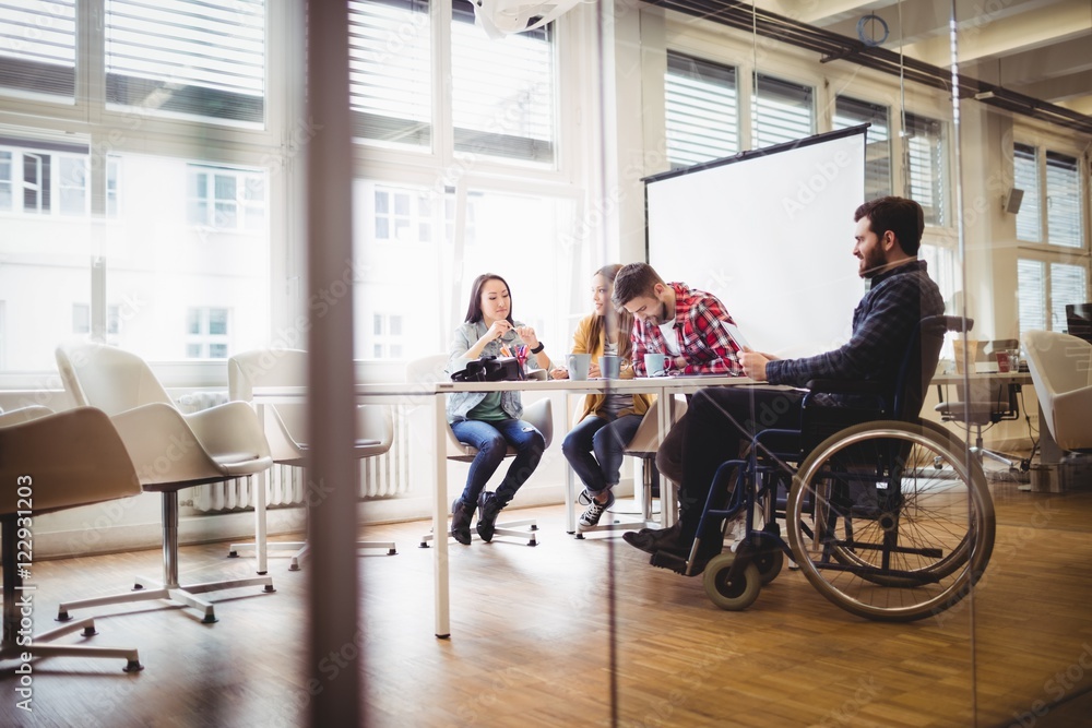 Coworker on wheelchair with photo editors in meeting room Coworker on wheelchair with photo editors in meeting room