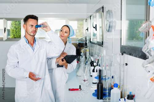 Two researchers in white coat checking wine acidity in laboratory