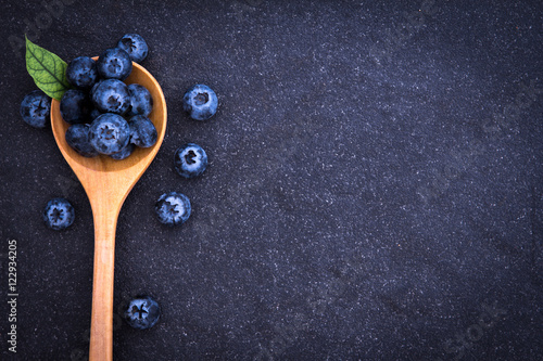  fresh picked blueberries in wooden spoon on black stone background