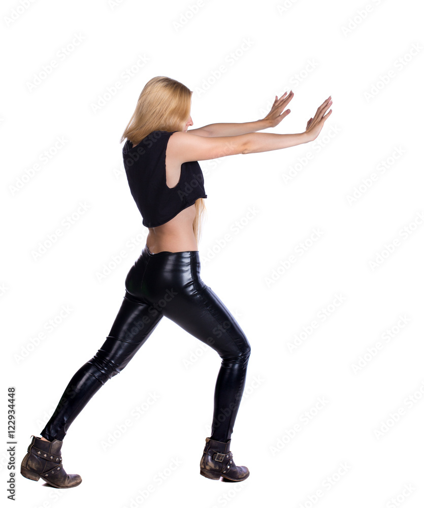 back view of woman pushes wall.  Isolated over white background. Rear view people collection. backside view of person. Blonde in leather pants shoves something in the side.