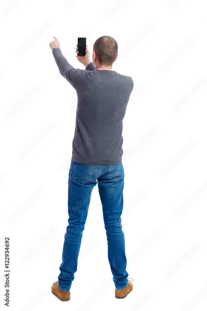 back view of standing young man and using a mobile phone. girl watching. Rear view people collection. backside view of person. Isolated over white background. A guy in a gray sweater photographs back view of standing young man and using a mobile phone. girl watching. Rear view people collection. backside view of person. Isolated over white background. A guy in a gray sweater photographs