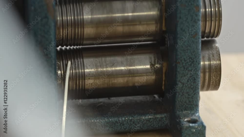 Tilt down of male hands pushing metal thing between the rollers of jewellery rolling mill Tilt down of male hands pushing metal thing between the rollers of jewellery rolling mill