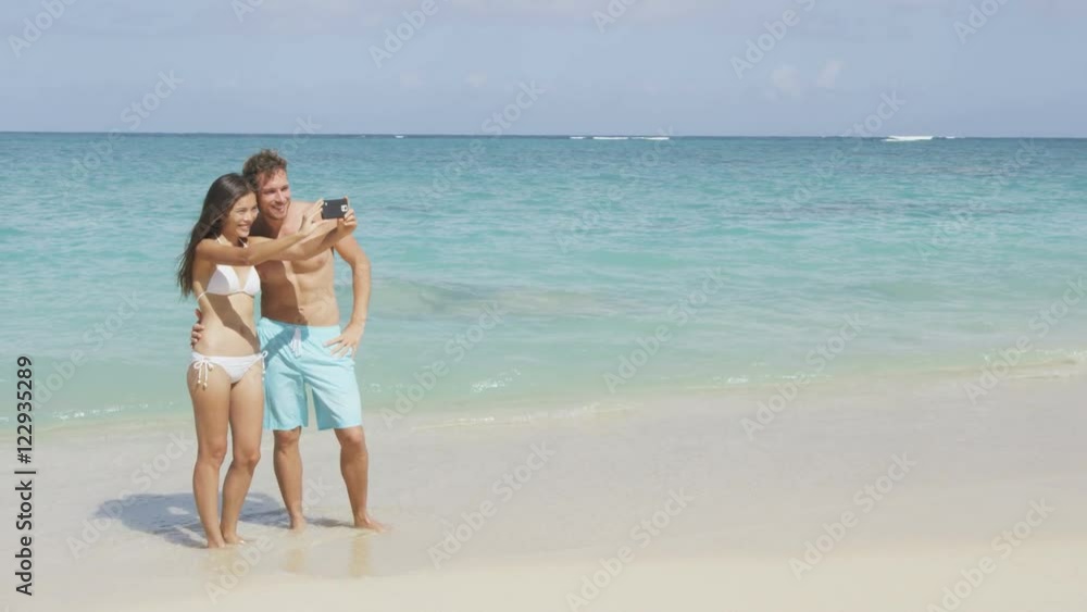 Beach vacation couple taking selfie photo with smart phone having fun using smartphone camera. Young beautiful Asian Caucasian couple taking self portrait photograph. RED EPIC SLOW MOTION 96 FPS. Beach vacation couple taking selfie photo with smart phone having fun using smartphone camera. Young beautiful Asian Caucasian couple taking self portrait photograph. RED EPIC SLOW MOTION 96 FPS.