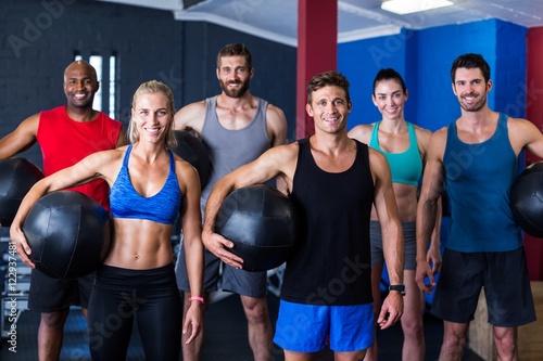 Portrait of smiling friends holding exercise ball in gym