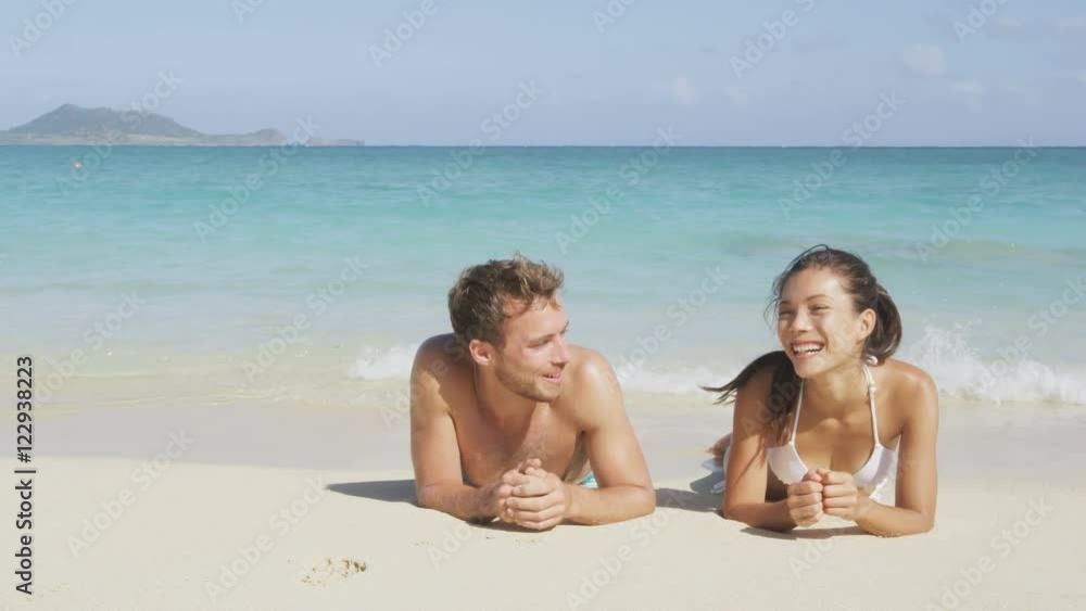 Couple in love relaxing on beach during vacation travel. Happy couple portrait talking together in a relationship sun tanning lying on the sand having fun in on Lanikai beach, Hawaii, United States. Couple in love relaxing on beach during vacation travel. Happy couple portrait talking together in a relationship sun tanning lying on the sand having fun in on Lanikai beach, Hawaii, United States.