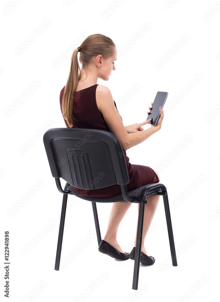 back view of woman sitting on chair and looks at the screen of the tablet. Rear view people collection. backside view of person. Isolated over white background. A girl in a burgundy dress sitting back view of woman sitting on chair and looks at the screen of the tablet. Rear view people collection. backside view of person. Isolated over white background. A girl in a burgundy dress sitting