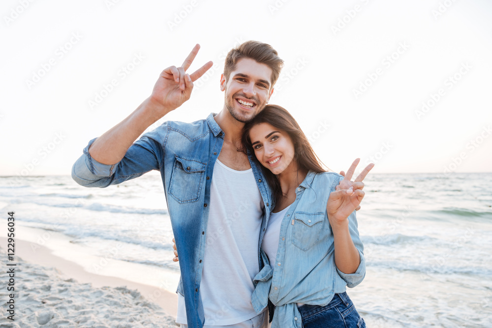 Cheerful young couple showing peace sign on the beach