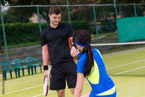 Male tennis player helps his female partner to stand up