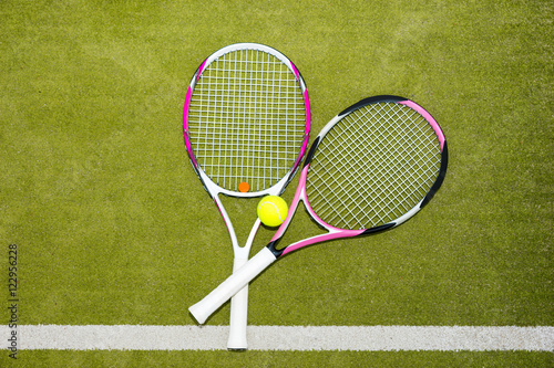 Two new pink tennis rackets with a tennis ball on a green grass