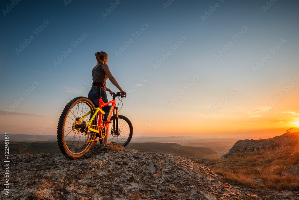 Obraz premium Sunset from the top / A woman with a bike enjoys the view of sunset over an autumn forest