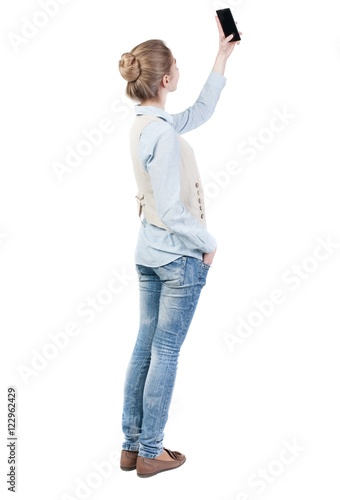 back view of standing young beautiful woman and using a mobile phone. girl watching. Rear view people collection. backside view of person. Isolated over white background.