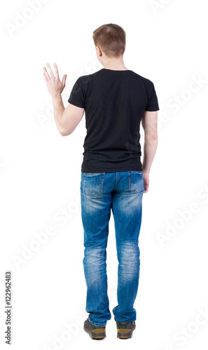 Back view of handsome man in t-shirt greeting waving from his hands. Standing young guy in jeans. Rear view people collection. backside view of person. Isolated over white background. guy in a vest