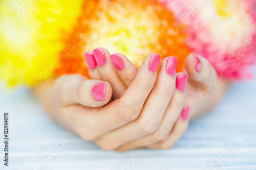 Woman cupped hands with pink manicured fingernails and bright multi colored flowers