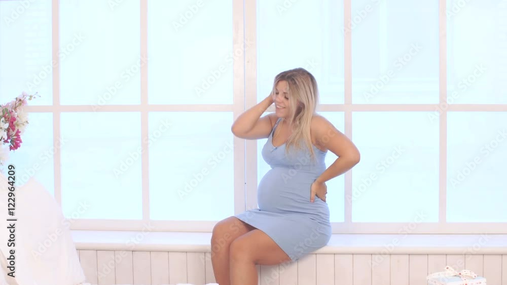 pregnant woman in blue dress sitting near the window pregnant woman in blue dress sitting near the window