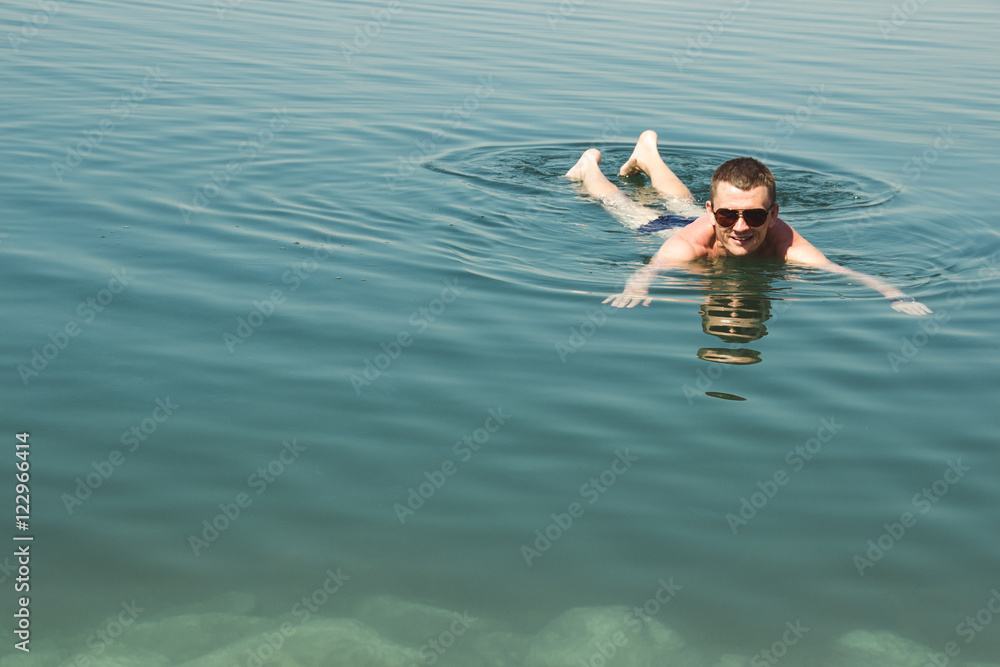 Man lying face-down position at Dead Sea enjoying vacation. Tourism recreation, healthy lifestyle concept. Copy space