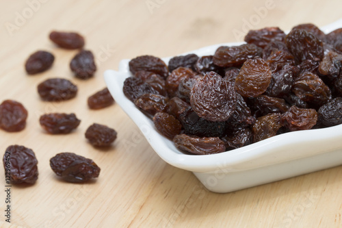 raisins in saucer on wooden table.