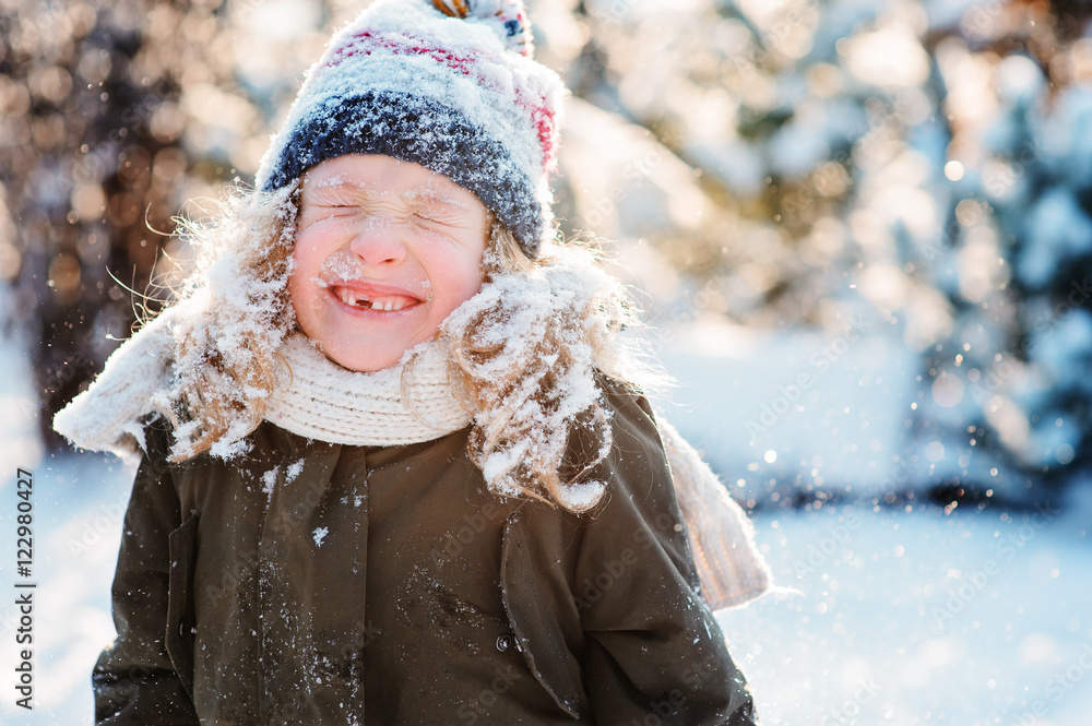 Obraz premium close up winter portrait of happy kid girl all covered with snow on the walk in winter snowy forest or garden. Seasonal outdoor activities.