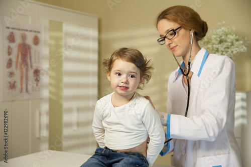 Cute little girl and doctor. Pediatrician woman examining cute little girl with stethoscope. Kid looks healthy and happy