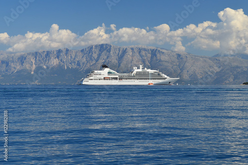 Big white cruiser ship in calm blue sea, high mountains on the background, blue sky with white clouds