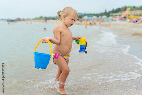 Adorable toddler girl playing with beach toys on white sand beach