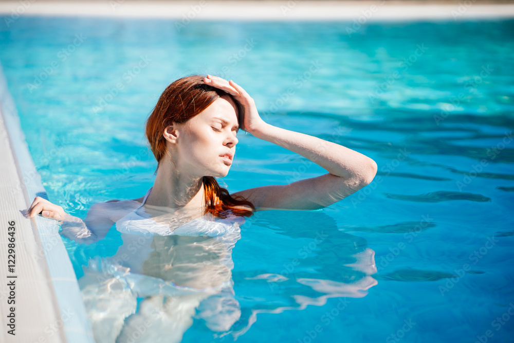 Beautiful young woman refreshing at summer swimming pool
