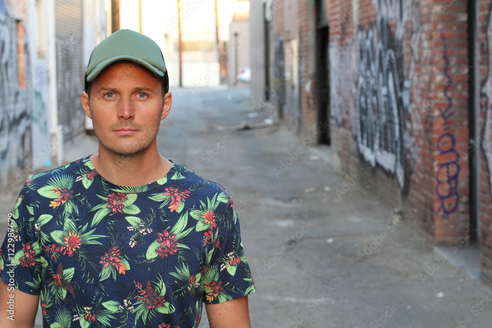 Athletic guy in a floral tee shirt and a baseball cap on urban background with copy space 