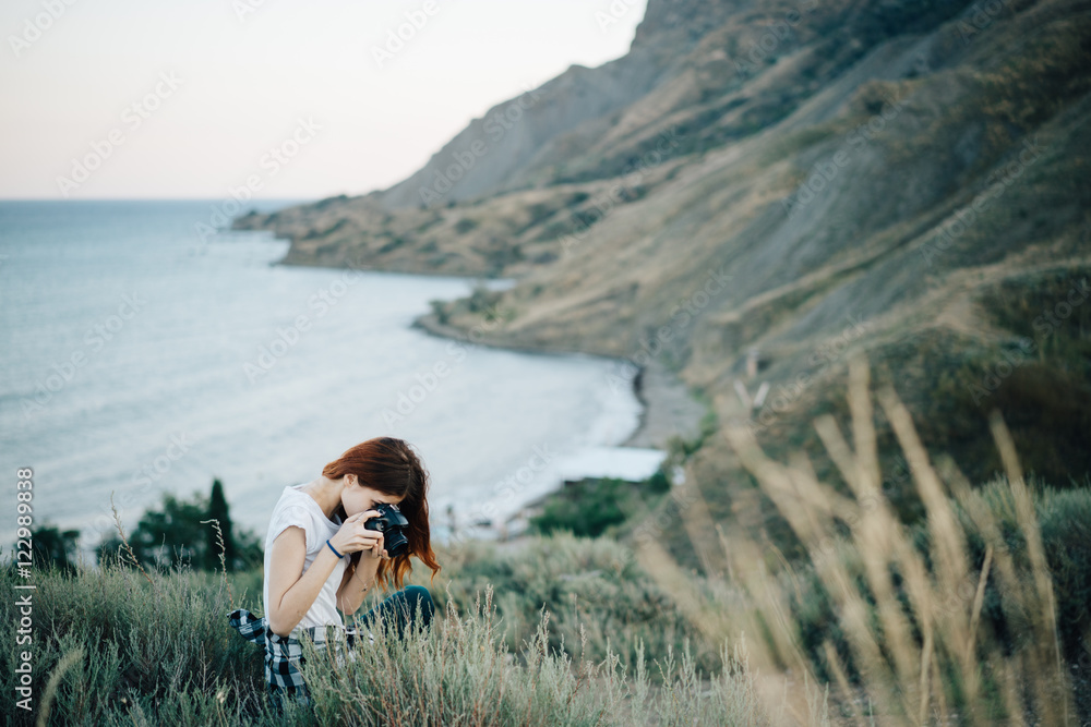 Woman sitting by the sea in the mountains with a camera
