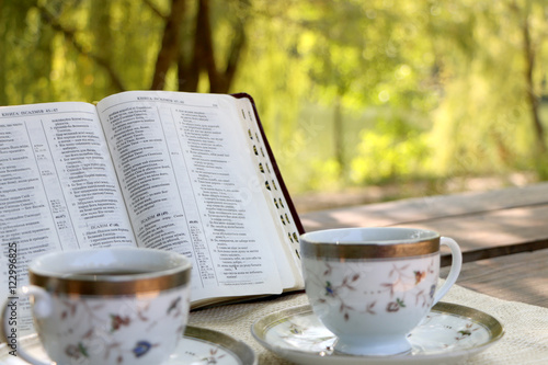  open book, two design cups of coffee on the wooden table in sunny day in the forest 