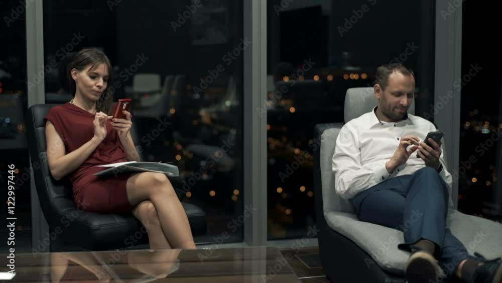 Young couple at home using smartphones sitting on armchairs by window at night
Young couple at home using smartphones sitting on armchairs by window at night