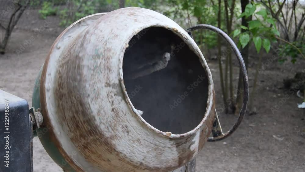 Close-up of spinning concrete mixer. Water is poured into the concrete mixer with bucket. Close-up of spinning concrete mixer. Water is poured into the concrete mixer with bucket.
