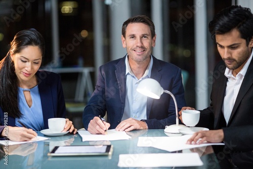 Businessman smiling at camera while colleagues writing on paper