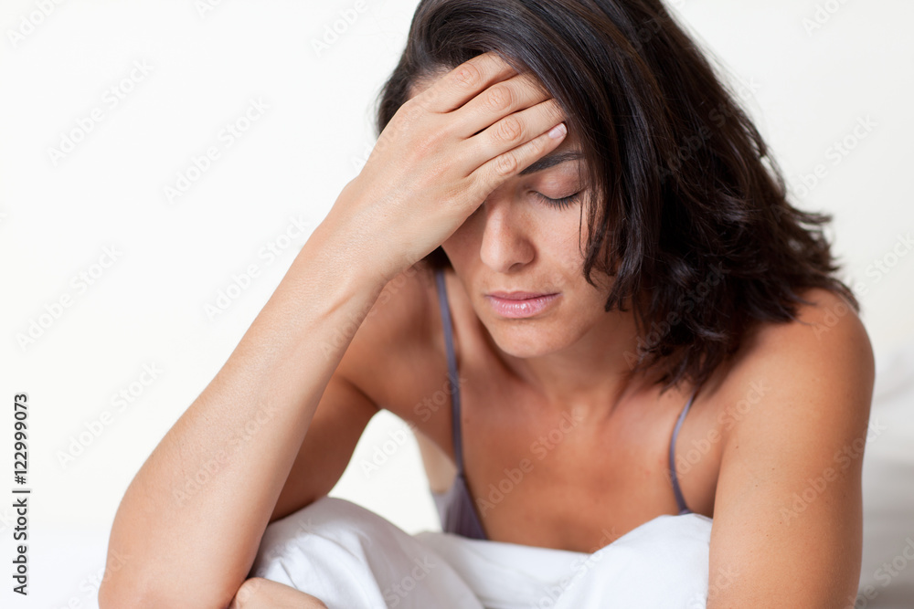 Hispanic woman with headache sitting in bed Hispanic woman with headache sitting in bed