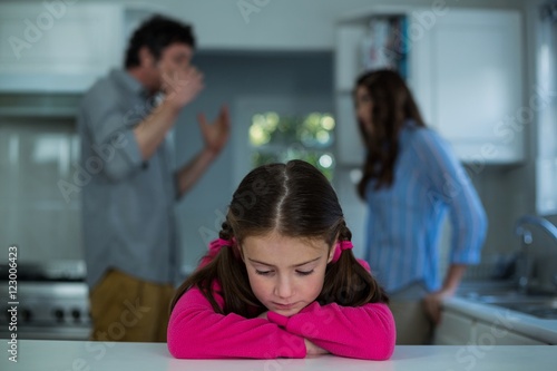 Upset girl sitting while couple having argument in background