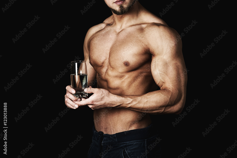 inflated healthy young man , holding a glass of water . A healthy way of life . On a dark background . inflated healthy young man , holding a glass of water . A healthy way of life . On a dark background .